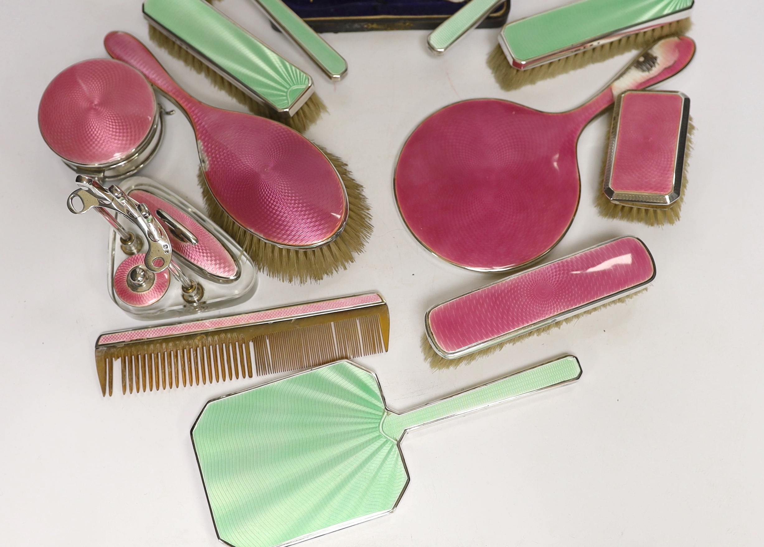 A 1930's five piece silver and green enamel mounted mirror and brush set by Mappin & Webb, a 1920's six piece silver and pink enamel mirror and brush set and two part manicure sets.